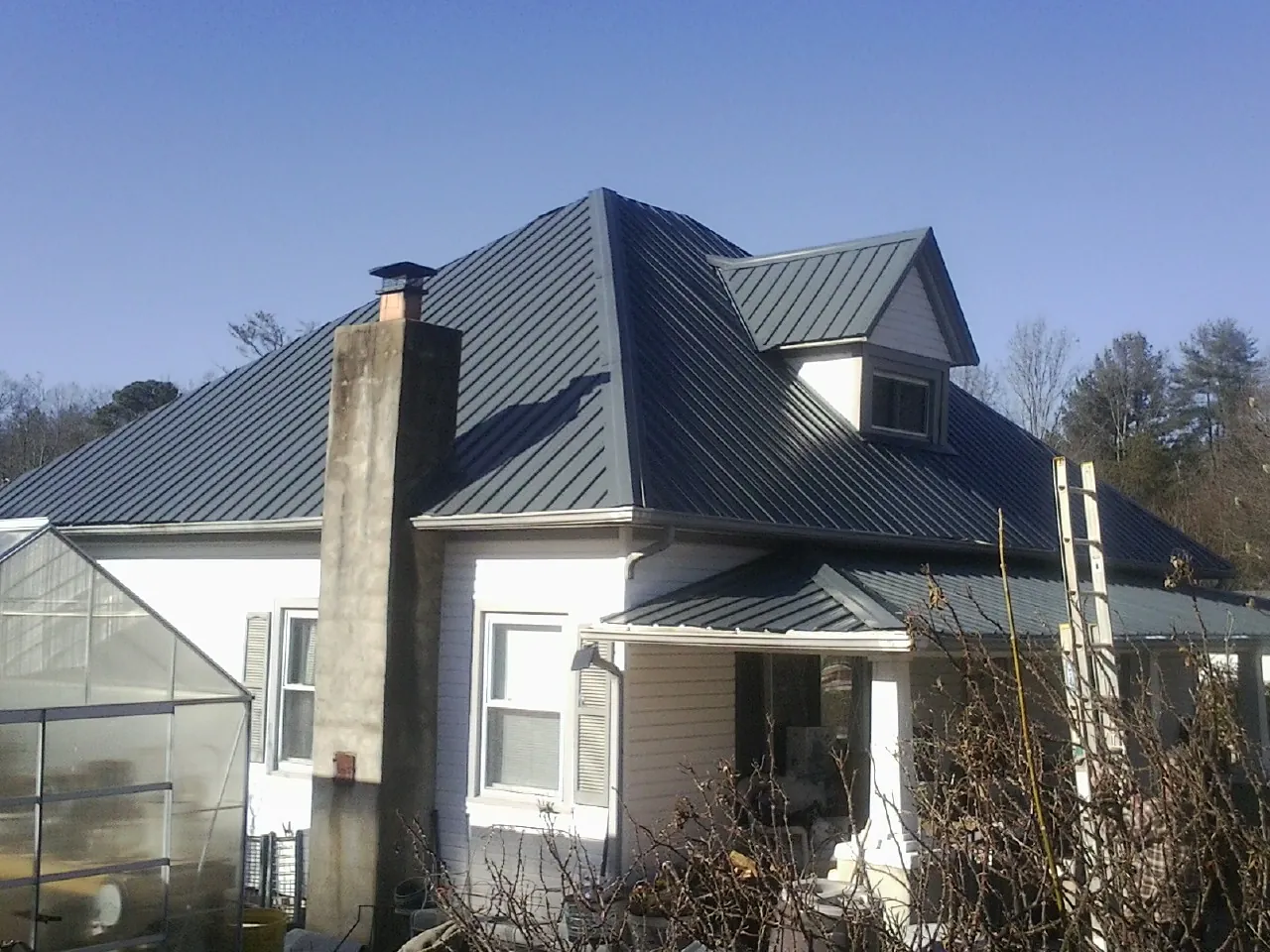 Dark blue standing seam metal roof on a white farmhouse with dormer in Duncanville