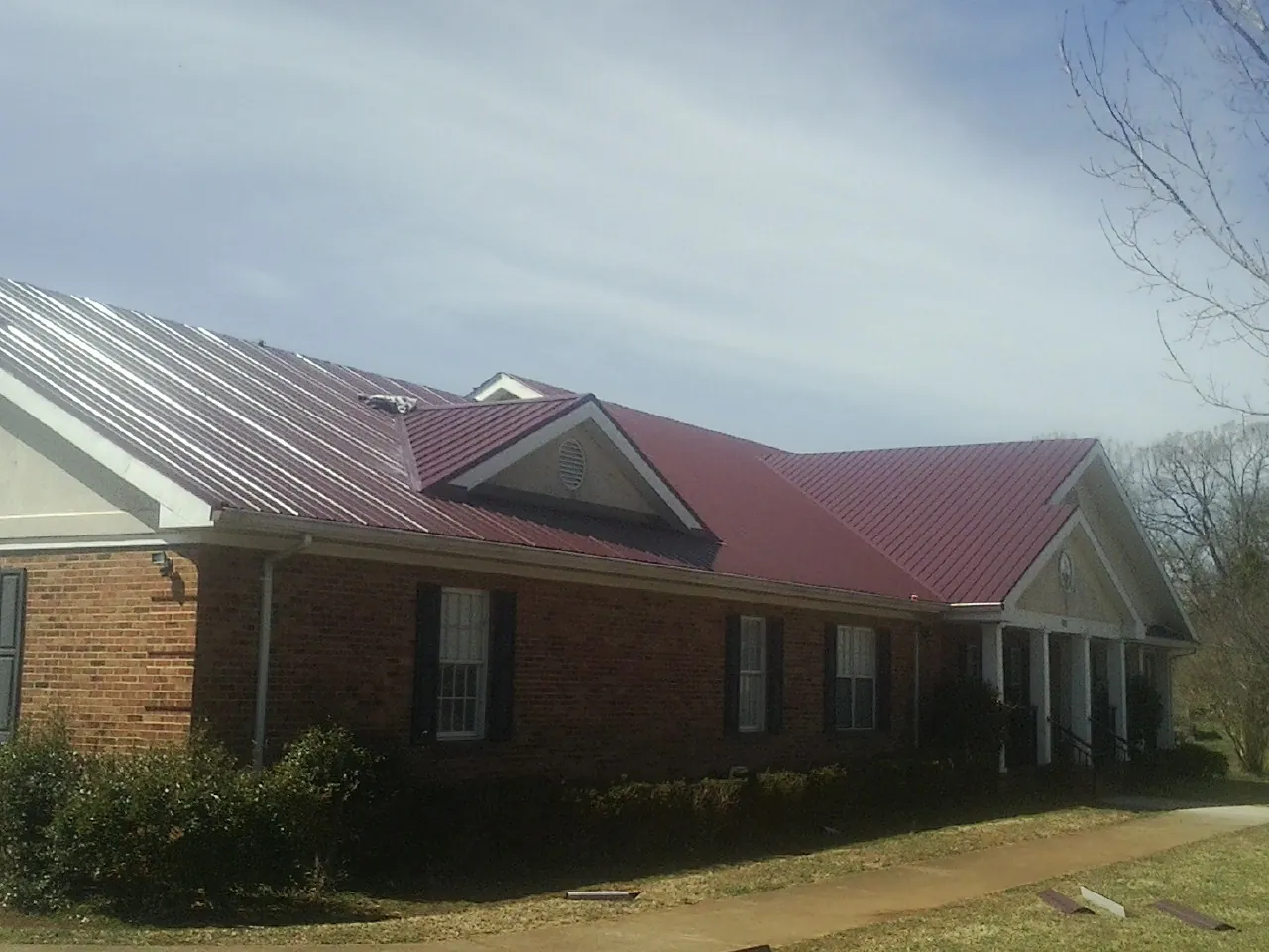 Red metal roof with gabled entries on a long brick building, from a Hail Damage Roof Repair job in Duncanville