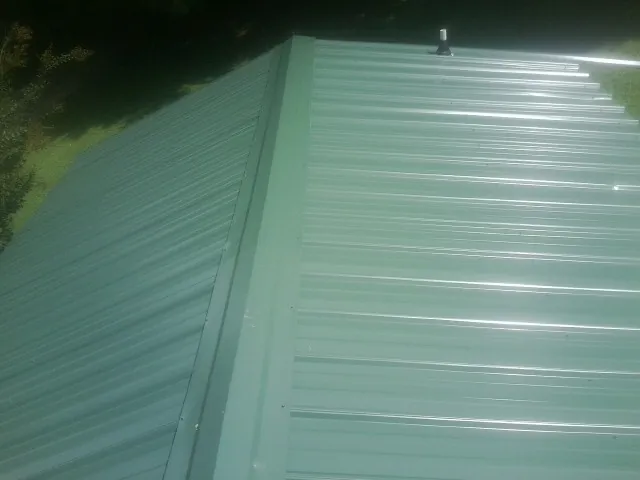 New green metal panels meeting at the ridge of a roof — Flat Roof Repair work by our crew in Duncanville