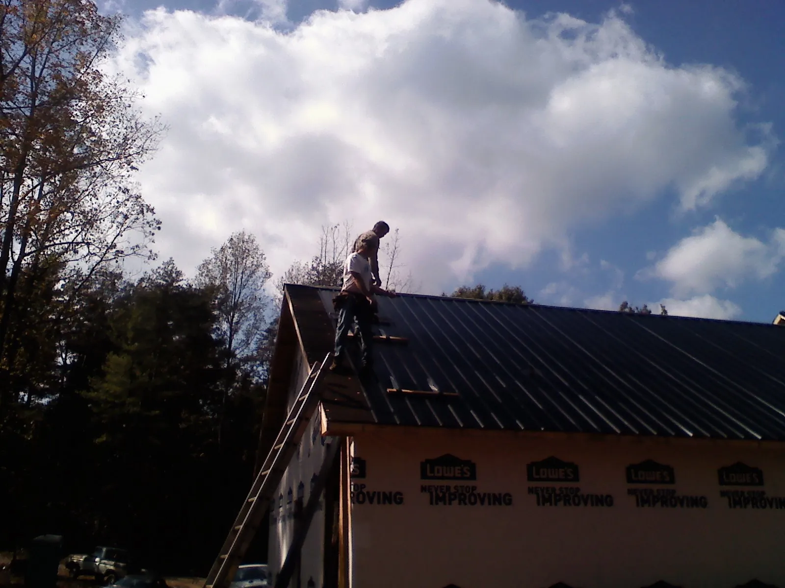 Roofer fastening dark metal panels high against a cloudy sky, from a Roof Inspection job in Duncanville